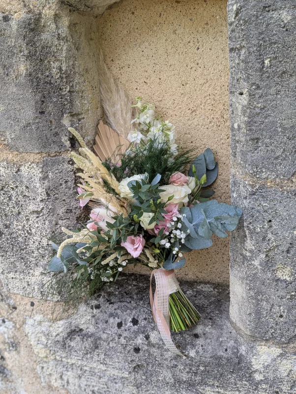 Sophisticated rustic bridal bouquet with roses, eucalyptus and pampas grass, resting on a stone wall.