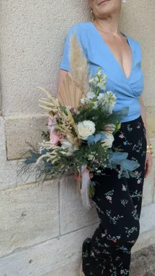 Elegantly rustic bridal bouquet with roses, eucalyptus and pampas grass, resting on a stone wall.