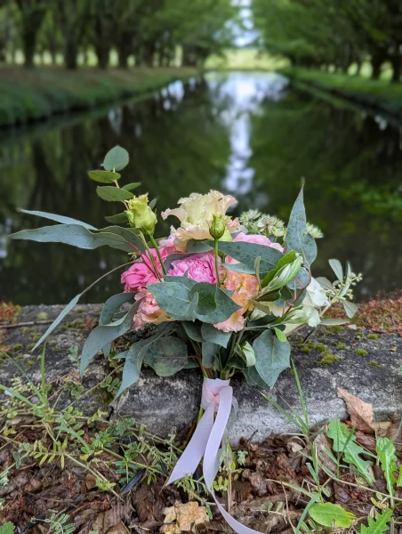 Bouquet de mariée romantique organique avec roses, lisianthus et eucalyptus, posé près d'un canal.