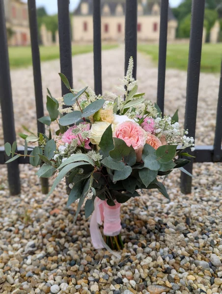 Bouquet de mariée romantique organique avec roses, lisianthus et eucalyptus, devant un château.