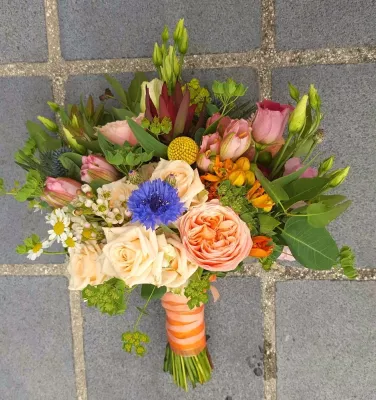 Bouquet de mariée champêtre, avec des roses pêches, de l'eustoma rose, des bleuets, du chardon bleu et du craspedia.