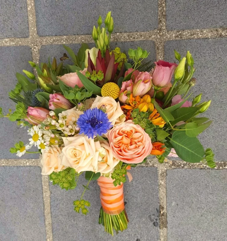 Bouquet de mariée champêtre, avec des roses pêches, de l'eustoma rose, des bleuets, du chardon bleu et du craspedia.