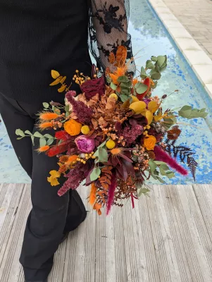Large sophisticated rustic bridal bouquet with orange roses, terracotta dried flowers, and red ferns.