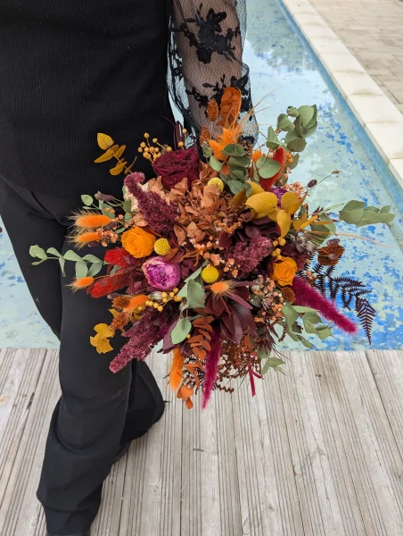Grand bouquet de mariée champêtre sophistiqué avec roses orange, fleurs séchées terracotta et fougères rouges.