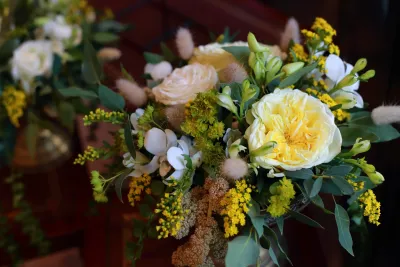 Gros plan d'un bouquet de mariée bohème avec roses jaunes et blanches, freesias et feuillage vert.