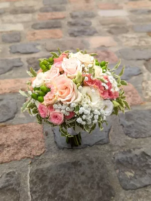 Bouquet de mariee champetre avec roses roses, blanches, gypsophile et baies vertes pour un mariage estival.
