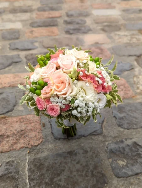 Bouquet de mariee champetre avec roses roses, blanches, gypsophile et baies vertes pour un mariage estival.