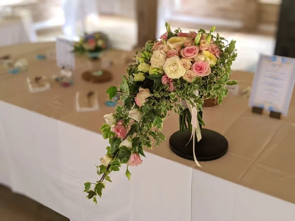 Magnifique bouquet de mariée en cascade de style bohème, composé de roses roses, crème et jaunes, avec un élégant lierre retombant.