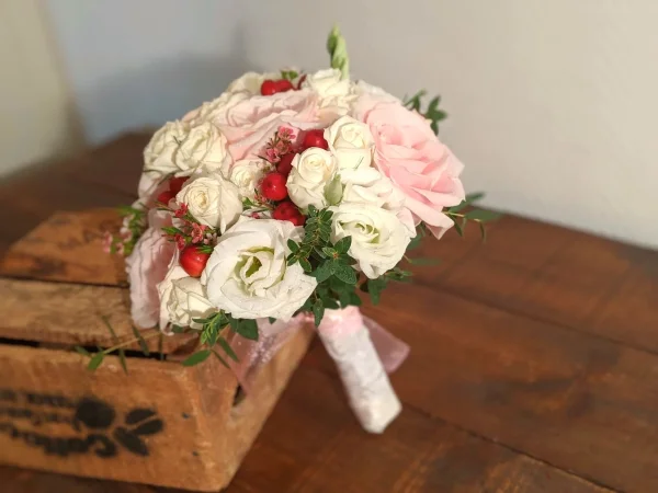 Bouquet de mariée classique avec des roses rose pâle et des lisianthus blancs, agrémenté de baies rouges pour un mariage d'automne.