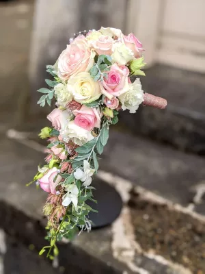 Élégant bouquet de mariée en cascade avec roses crème, roses roses, lisianthus blancs et feuillage, perles décoratives.