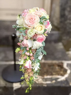 Magnifique bouquet de mariée tombant avec roses variées, lisianthus et callas blanches, orné de perles fines et feuillage.