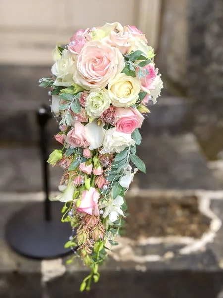 Magnifique bouquet de mariée tombant avec roses variées, lisianthus et callas blanches, orné de perles fines et feuillage.