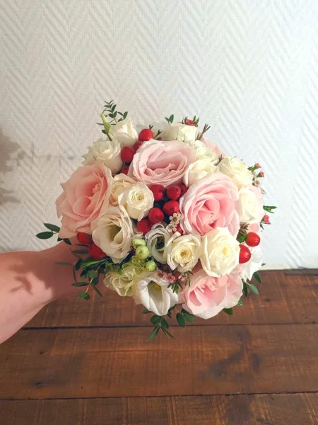 Bouquet de mariée romantique et classique, composé de roses rose et lisianthus blancs, avec des accents de baies rouges.