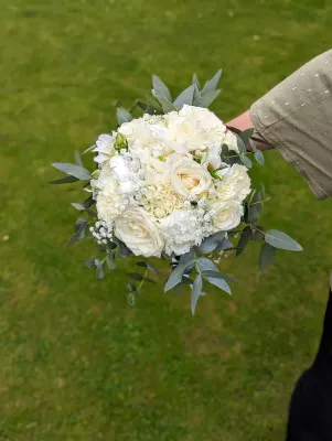 Bouquet de mariée rond composé de roses, œillets blancs, gypsophile et eucalyptus, style classique et frais.