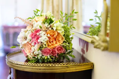 A garden-style bridal bouquet featuring peach-orange roses, coral roses, gypsophila, and verdant green foliage.