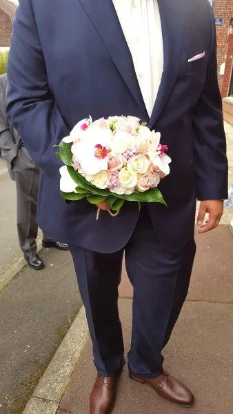 Bouquet de mariée rond style classique avec roses crème, roses poudrées, orchidées blanches et feuillage vert pour un mariage estival.