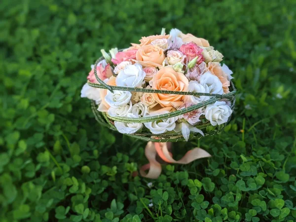 Bouquet de mariée de style exotique avec roses pêche et blanches, eustoma et feuillage discret pour un mariage