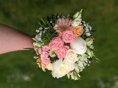 Vue de dessus d'un bouquet de mariée champêtre, composé de roses roses et pêche, pivoines crème et lisianthus blancs, avec feuillage varié.