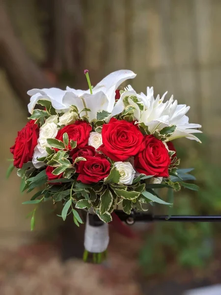 Bouquet de mariée classique avec roses rouges et blanches, lys blancs, et feuillage panaché pour un mariage à Saint-Aubin-de-Médoc.