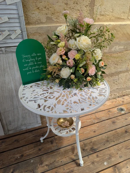 Grand bouquet champêtre pour plan de table de mariage, avec roses crème, alstroemeria rose et feuillage vert sur table blanche.