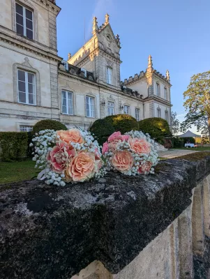 Deux bouquets à lancer champêtres composés de roses pêche, roses poudré et gypsophile blanc, posés devant un château.