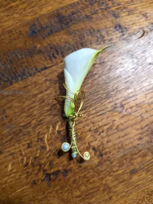 Boutonnière minimaliste pour un marié, avec un arum blanc élégamment rehaussé de fil d'or et de perles délicates.