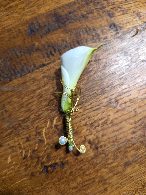 Boutonnière minimaliste pour un marié, avec un arum blanc élégamment rehaussé de fil d'or et de perles délicates.