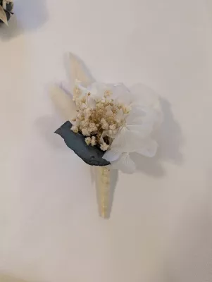Boutonnière ou corsage de mariage avec une fleur blanche délicate, du gypsophile, des éléments séchés et une touche de feuillage.