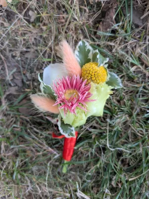 Boutonnière champêtre sophistiquée avec dahlia fuchsia, craspedia jaune et feuillage panaché.