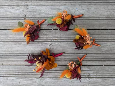 Sophisticated rustic buttonholes with dried orange, red, and yellow flowers, burgundy foliage for wedding.