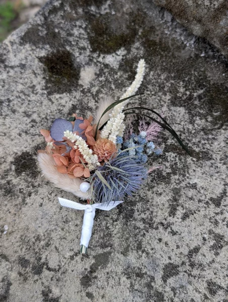Bohemian botanical buttonhole with dried orange flowers, blue thistle, and green foliage.