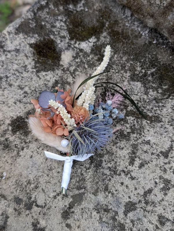 Bohemian botanical buttonhole with dried orange flowers, blue thistle, and green foliage.