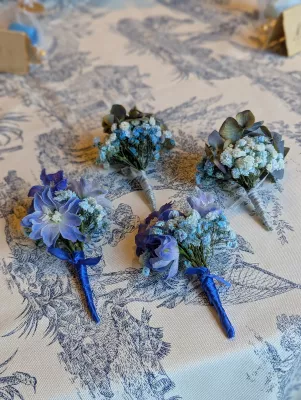 Boutonnière classique mariage avec gypsophila bleue, campanules et feuilles vertes, attachée d'un ruban satiné bleu.