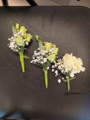 Trois boutonnières de mariage classiques avec gypsophile et lisianthus, ruban vert, parfaites pour un événement élégant.