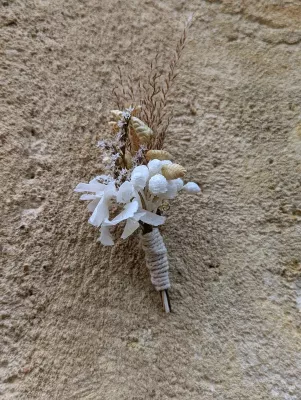 Boutonnière bohème élégante avec herbes séchées naturelles et petites fleurs blanches pour un mariage d'automne.