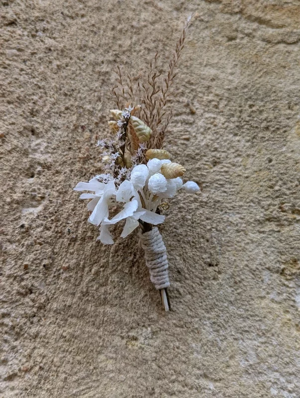 Elegant bohemian buttonhole with natural dried grasses and small white flowers for an autumn wedding.