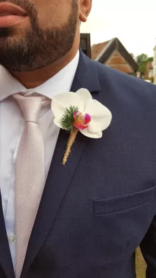 Boutonnière de marié style classique avec une orchidée blanche à cœur magenta, feuillage vert et lien en ficelle naturelle.