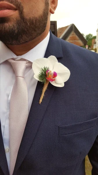 Boutonnière de marié style classique avec une orchidée blanche à cœur magenta, feuillage vert et lien en ficelle naturelle.