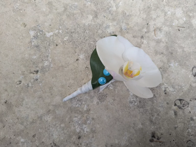 Minimalist buttonhole with a white orchid, a green leaf, and blue beads.