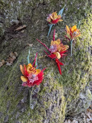 Boutonnière exotique vibrante avec petites orchidées orange, éléments rouges et touches de fuchsia sur un fond de mousse verte.