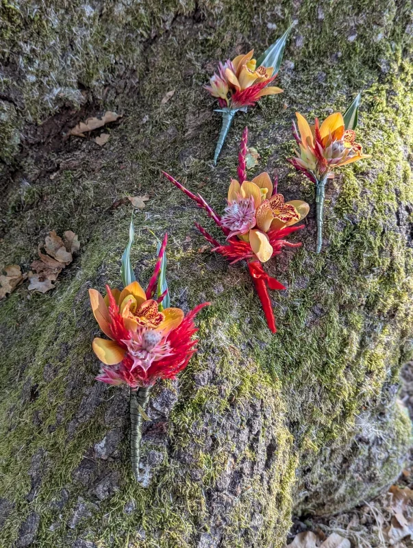 Vibrant exotic buttonhole with small orange orchids, red accents, and touches of fuchsia on a background of green moss.