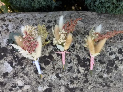 Three bohemian botanical buttonholes featuring pampas grass and pink and white dried flowers for a wedding.