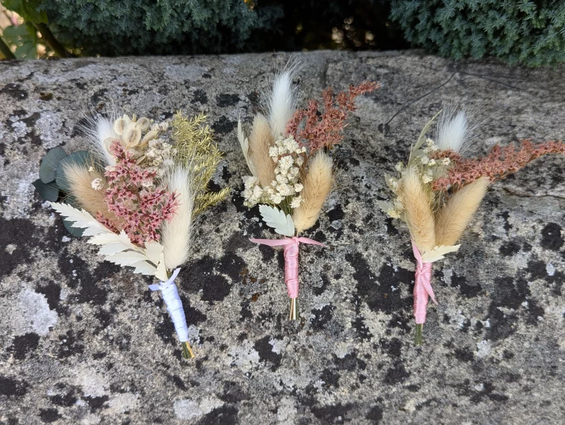 Three bohemian botanical buttonholes featuring pampas grass and pink and white dried flowers for a wedding.