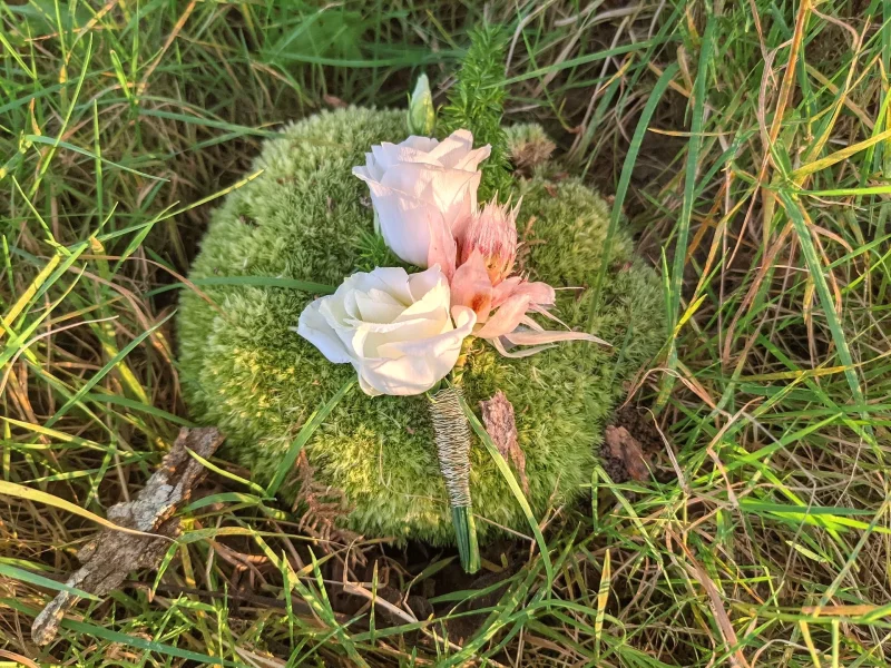 Boutonnière exotique et élégante avec une rose blanche et une petite fleur rose pour un mariage d'automne