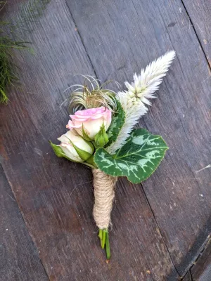 Boutonnière champêtre avec roses pâles, celosie et feuillage vert, attachée avec de la cordelette de jute pour un mariage.