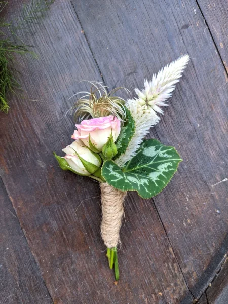 Boutonnière champêtre avec roses pâles, celosie et feuillage vert, attachée avec de la cordelette de jute pour un mariage.