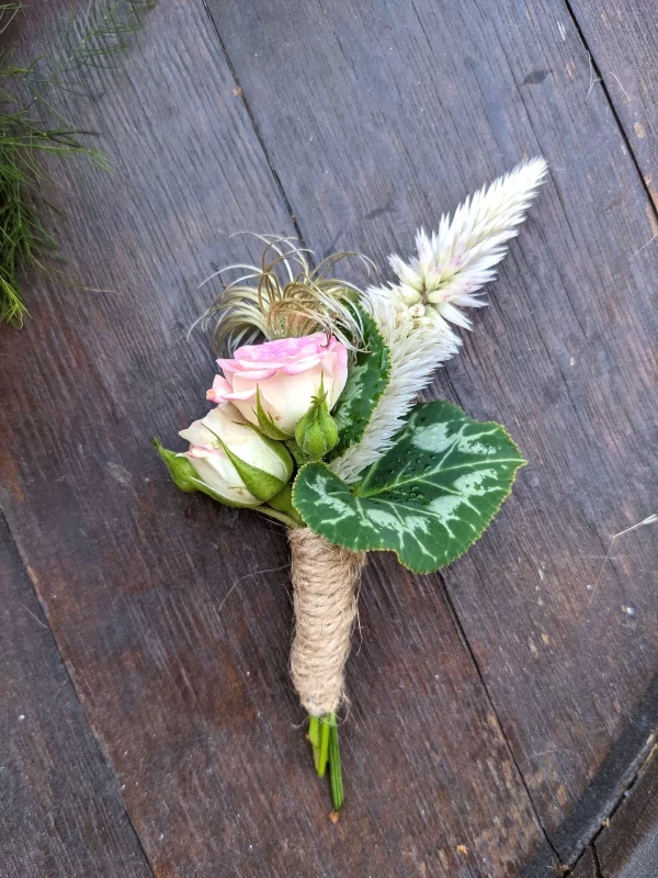 Rustic-chic buttonhole featuring pale roses, celosia and green foliage, tied with jute twine for a wedding.