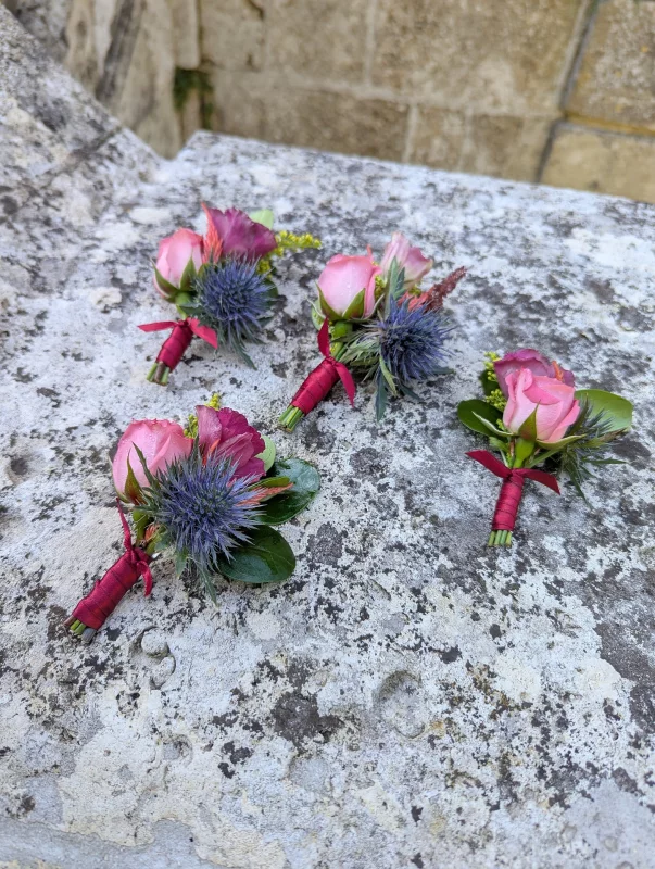 Boutonnière champêtre raffinée avec une rose rose délicate et un chardon bleu-violet, parfait pour les mariés et les témoins.