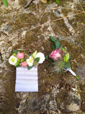 Deux boutonnières de mariage de style champêtre, une avec roses blanches et roses, l'autre avec une rose unique et chardon.