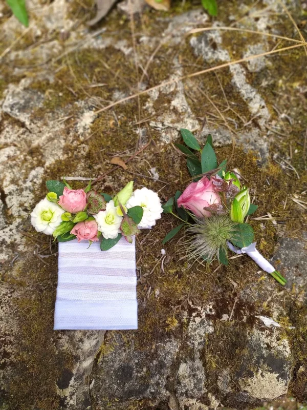 Two country-style wedding buttonholes, one with white and pink roses, the other with a single rose and thistle.